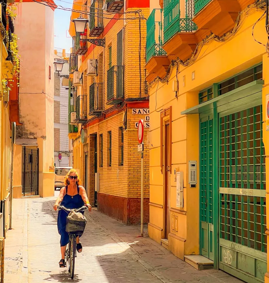 A cyclist on a yellow street in the old centre of Seville, green balconies overhead