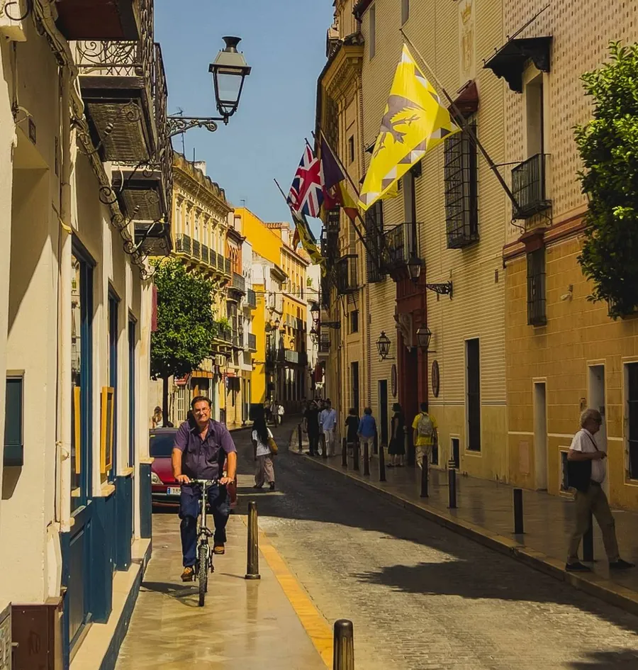 A morning street in the old centre of Seville, a cyclist under the balconies and flags