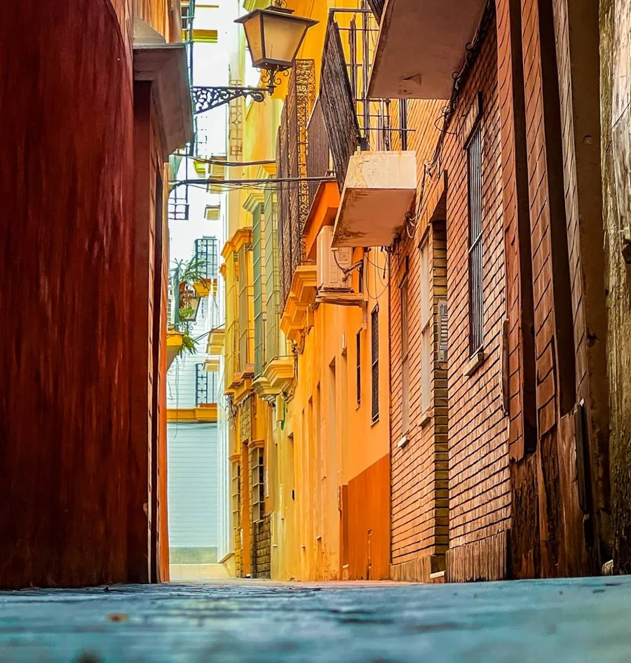 A narrow ochre street in the old centre of Seville, lantern and balconies overhead